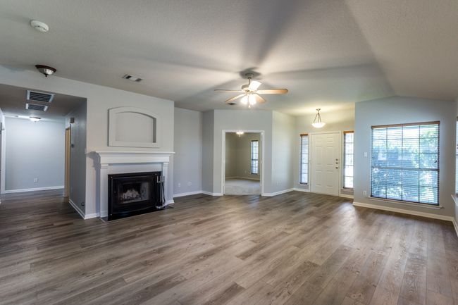 Unfurnished living room with a fireplace with flush hearth, wood finished floors, ceiling fan, a textured ceiling, and lofted ceiling | Image 4