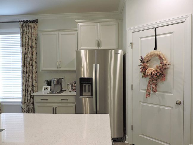 Kitchen with stainless steel fridge, white cabinetry, crown molding, and light stone countertops | Image 7
