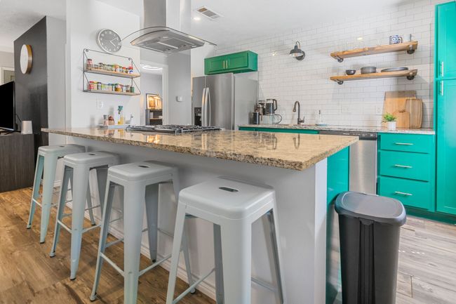 Kitchen featuring appliances with stainless steel finishes, open shelves, island exhaust hood, and a breakfast bar | Image 11
