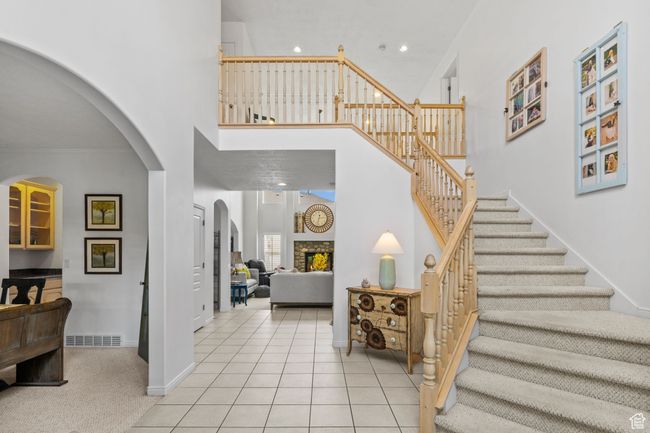Entrance foyer featuring visible vents, a towering ceiling, a fireplace, stairway, and arched walkways | Image 8