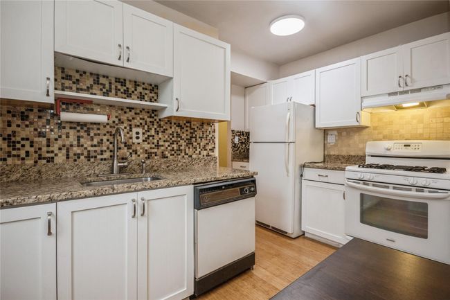 Kitchen with white appliances, under cabinet range hood, decorative backsplash, white cabinetry, and stone countertops | Image 5