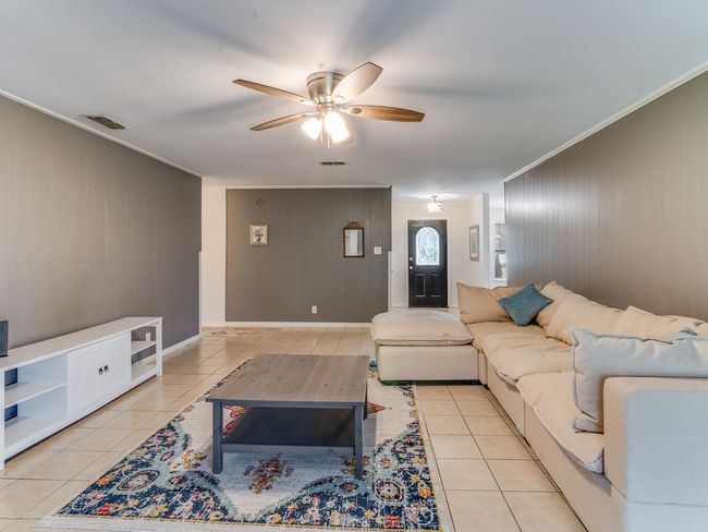 Living area with light tile patterned flooring, a ceiling fan, ornamental molding, wood walls, and an accent wall | Image 7