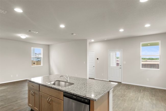 Kitchen featuring stainless steel dishwasher, light wood-type flooring, a kitchen island with sink, light stone countertops, and recessed lighting | Image 21