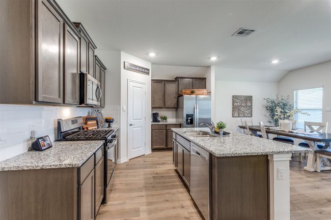 Kitchen View 5 featuring stainless steel appliances, light laminated wood plank floors, backsplash, and a center island with sink, and generous sized walk in corner pantry. | Image 11