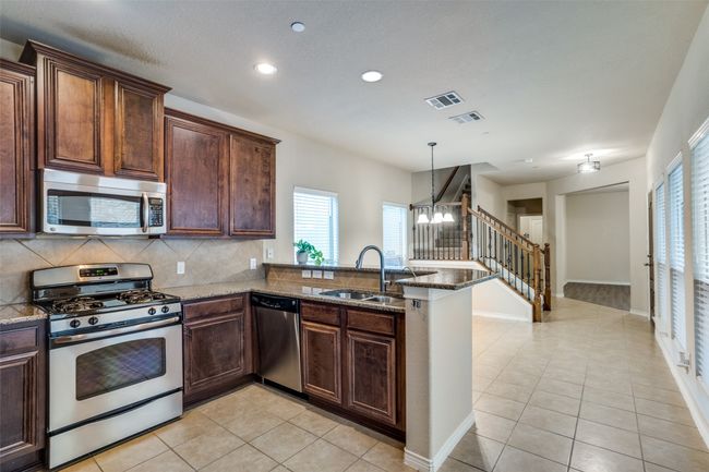 Kitchen featuring a sink, light tile floors, stone counters, appliances with stainless steel finishes, and recessed lighting | Image 8