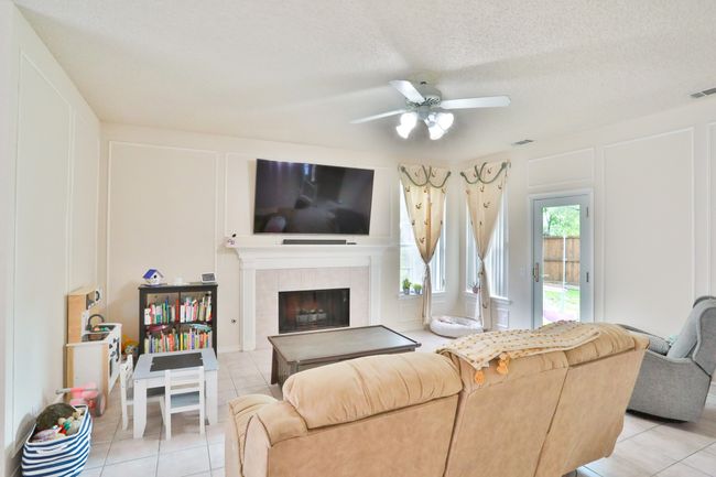 Living area featuring ceiling fan, light tile patterned floors, a tile fireplace, and a decorative wall | Image 9