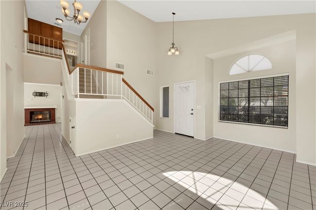 Foyer featuring light tile patterned floors, visible vents, an inviting chandelier, stairs, and a fireplace | Image 5