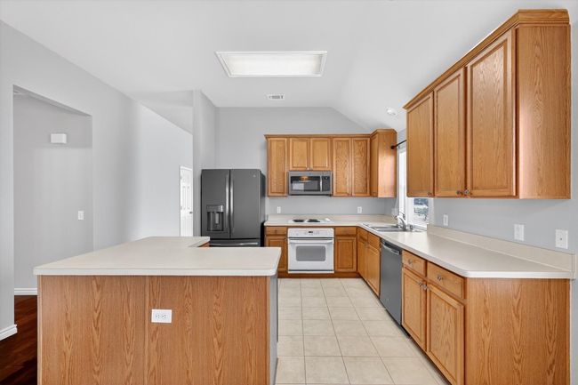 Kitchen featuring appliances with stainless steel finishes, lofted ceiling, light countertops, light tile patterned floors, and a center island | Image 8
