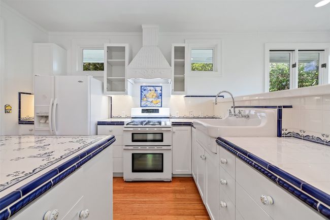 Kitchen featuring custom range hood, white cabinetry, white refrigerator with ice dispenser, a wealth of natural light, and range with two ovens | Image 9
