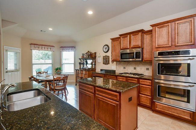 The kitchen features elegant wooden cabinetry, sleek granite countertops, modern stainless steel appliances, and a cozy dining area with abundant natural light. | Image 10