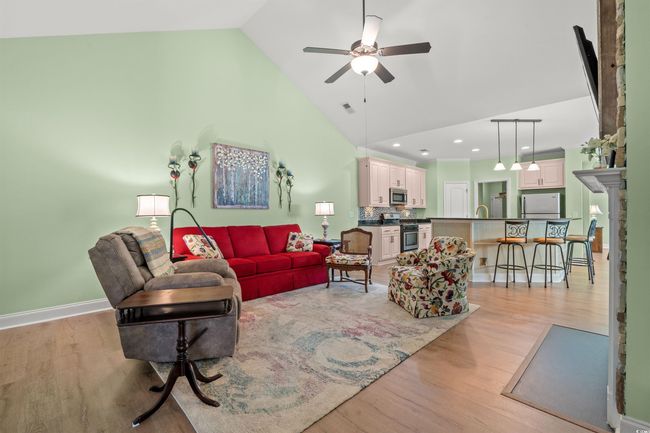 Living room with high vaulted ceiling, baseboards, light wood-style floors, visible vents, and ceiling fan | Image 12