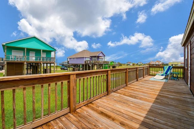 This photo showcases the back sun deck with a lounge chair and small table, perfect for relaxing. The area offers a clear view of a grassy landscape and neighboring houses, and bay views. | Image 23