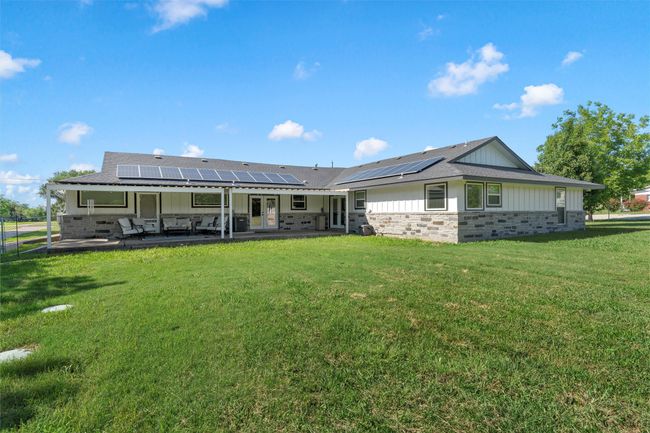 Rear view of house featuring board and batten siding, a patio area, a yard, roof mounted solar panels, and french doors | Image 26