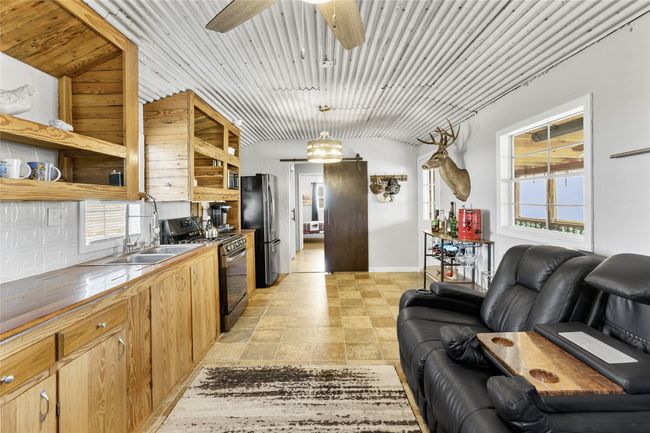 Kitchen featuring black gas stove, a ceiling fan, freestanding refrigerator, open shelves, and a sink | Image 5