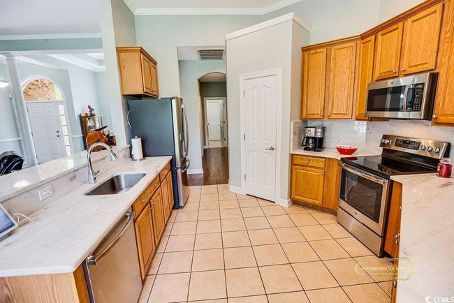 Kitchen featuring appliances with stainless steel finishes, ornamental molding, light tile patterned flooring, brown cabinetry, and backsplash | Image 14