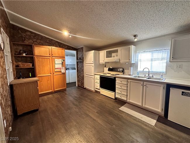 Kitchen with a textured ceiling, a sink, dark wood-style flooring, dishwasher, and range with electric stovetop | Image 8