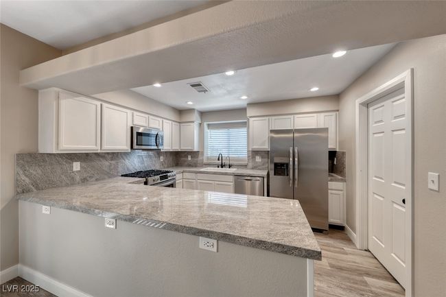 Kitchen featuring appliances with stainless steel finishes, a peninsula, backsplash, white cabinets, and recessed lighting | Image 11