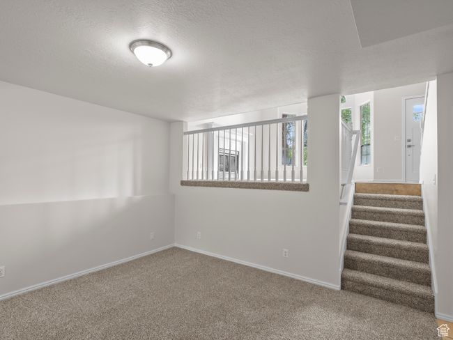 Carpeted empty room featuring a textured ceiling, baseboards, and stairway | Image 24