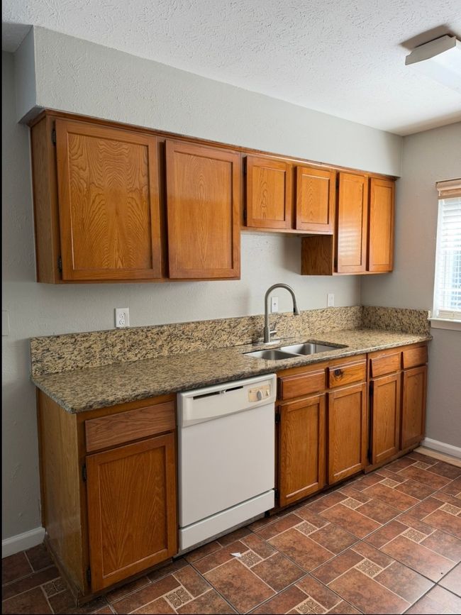 Kitchen with white dishwasher, brown cabinetry, stone countertops, and a textured ceiling | Image 9