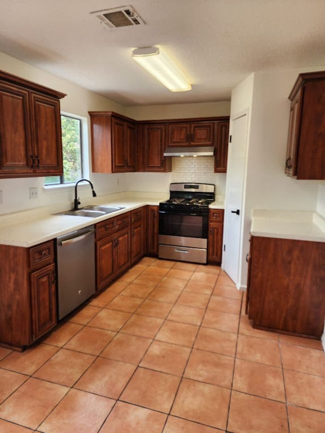 Kitchen with stainless steel appliances, light countertops, under cabinet range hood, backsplash, and light tile patterned floors | Image 4