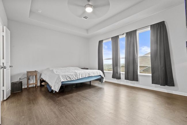 Bedroom featuring a tray ceiling, wood finished floors, baseboards, and ceiling fan | Image 19