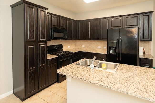 Kitchen featuring black appliances, a sink, decorative backsplash, light tile patterned floors, and light stone countertops | Image 34