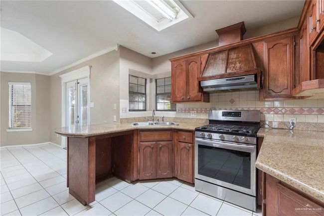 Kitchen with gas stove, a peninsula, backsplash, light tile patterned floors, and crown molding | Image 10