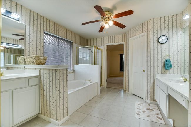 Full bathroom featuring wallpapered walls, ceiling fan, two vanities, a shower stall, and a bath | Image 12