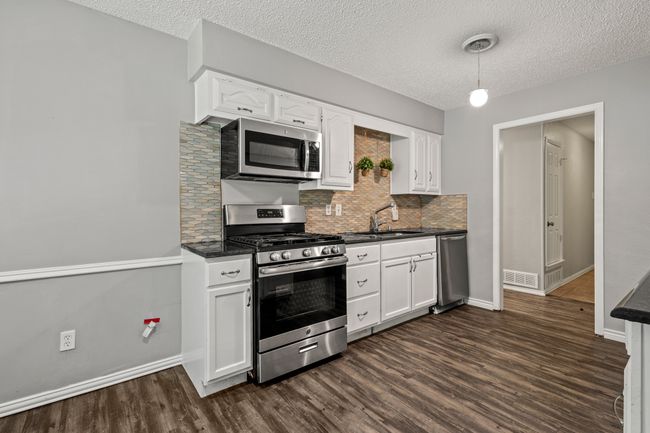 Kitchen with appliances with stainless steel finishes, a sink, dark countertops, dark wood-style floors, and tasteful backsplash | Image 5