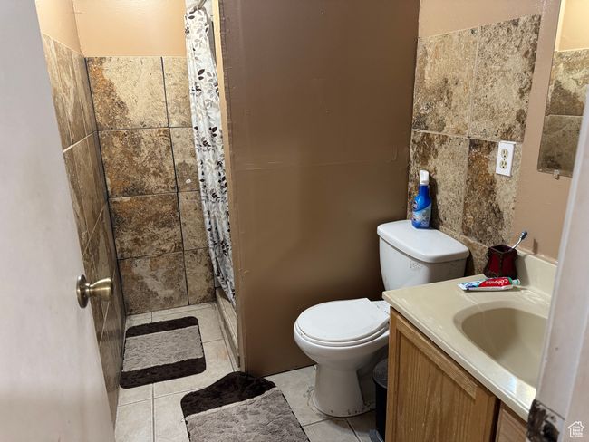 Full bath featuring a shower stall, tile patterned flooring, toilet, vanity, and tile walls | Image 12