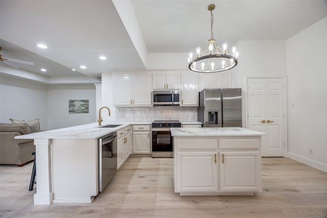Kitchen featuring stainless steel appliances, light wood-style flooring, open floor plan, backsplash, and a chandelier | Image 10