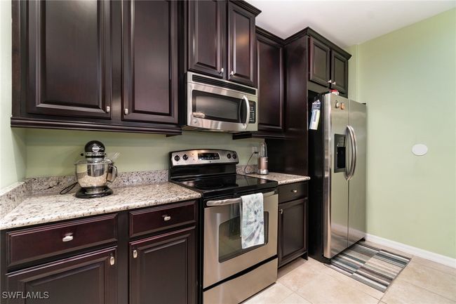 Kitchen with appliances with stainless steel finishes, dark brown cabinets, baseboards, light tile patterned flooring, and light stone countertops | Image 7