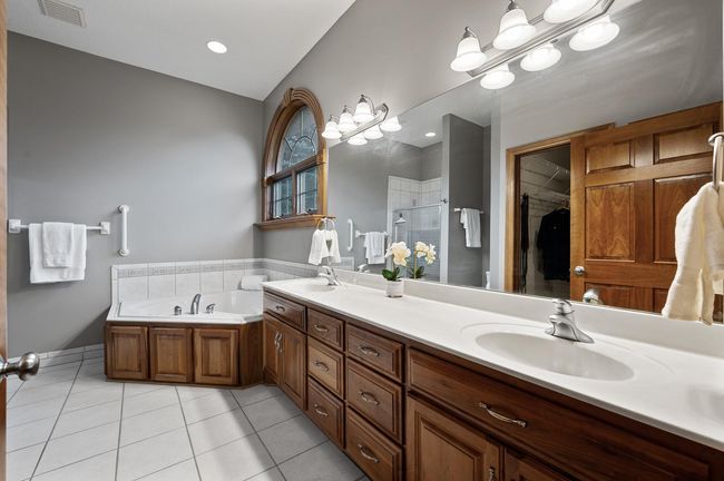 Private primary bath features a jetted soaking tub, ceramic tile floors, and dual vanities plus walk in closet access allowing for a comfortable reset each morning. | Image 18