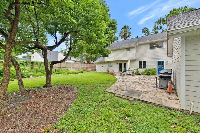 Welcome to your spacious backyard with a lush lawn and mature trees, featuring a stone patio perfect for outdoor dining and relaxation. | Image 5