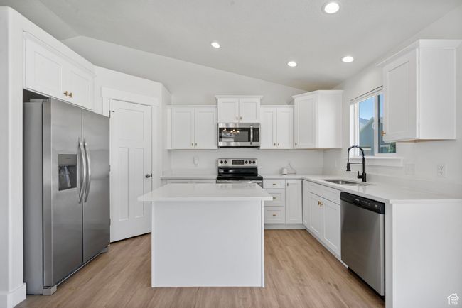Kitchen with appliances with stainless steel finishes, lofted ceiling, white cabinetry, light wood-style flooring, and a center island | Image 6