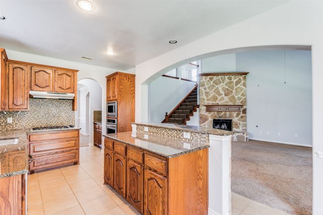 Kitchen featuring stainless steel appliances, arched walkways, under cabinet range hood, open floor plan, and stone countertops | Image 12