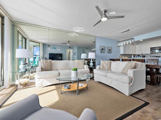 Living area with ceiling fan, a textured ceiling, wood finished floors, and a wall of windows | Image 4