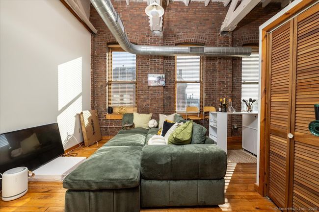 A stylish loft-style interior with exposed brick walls, high ceilings with industrial ductwork, polished hardwood floors, rustic wood doors, and a cozy open layout featuring large windows that bring in natural light | Image 4