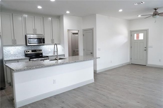 Kitchen featuring appliances with stainless steel finishes, a sink, tasteful backsplash, light stone counters, and light wood finished floors | Image 4