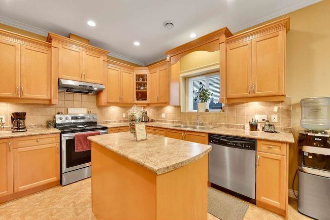 Kitchen with stainless steel appliances, under cabinet range hood, a sink, ornamental molding, and backsplash | Image 26