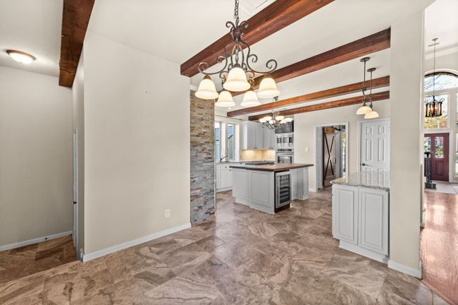 Kitchen featuring a chandelier, oven, beverage cooler, beamed ceiling, and white cabinetry | Image 12