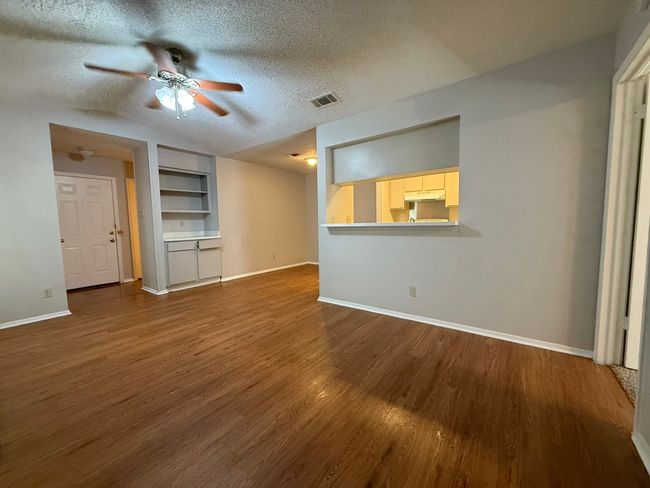 Unfurnished living room featuring a ceiling fan, dark wood-type flooring, a textured ceiling, and built in shelves | Image 4