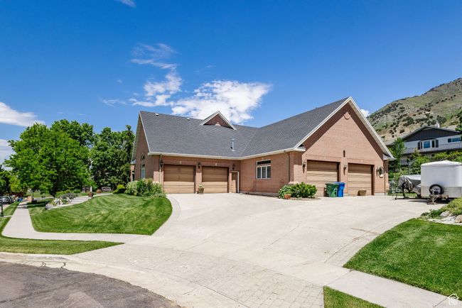 View of front of property featuring brick siding, a front lawn, an attached garage, a mountain view, and driveway | Image 74