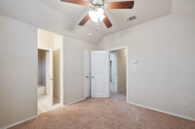 Unfurnished bedroom featuring light colored carpet, vaulted ceiling, ensuite bath, and a ceiling fan | Image 18