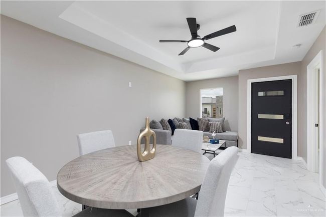Dining room featuring a raised ceiling, a ceiling fan, light marble finish flooring, and baseboards | Image 4