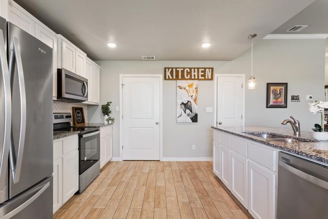 Kitchen with stainless steel appliances, white cabinetry, ornamental molding, dark stone countertops, and light wood-style floors | Image 15
