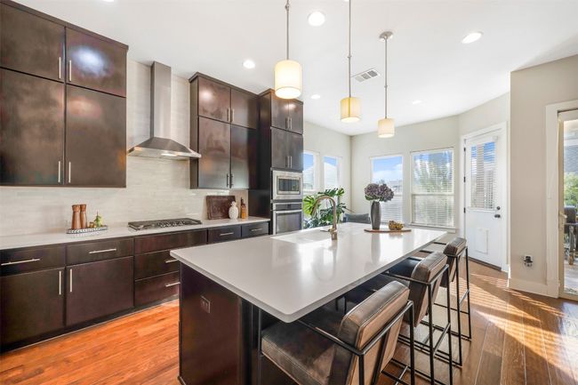 Kitchen featuring wall chimney range hood, stainless steel appliances, light wood-type flooring, a breakfast bar area, and recessed lighting | Image 25
