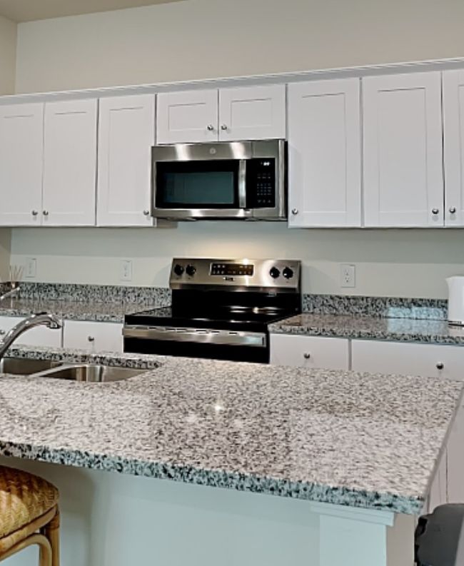 Kitchen with appliances with stainless steel finishes, white cabinetry, light stone countertops, and a kitchen breakfast bar | Image 11