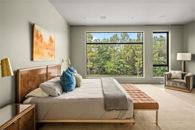 An alternate view of the expansive primary suite reveals a peaceful sitting area perfectly positioned to take in the lush, treetop scenery beyond the oversized windows. This cozy corner invites quiet mornings with coffee or a good book, blending comfort and natural beauty in one tranquil space. | Image 18