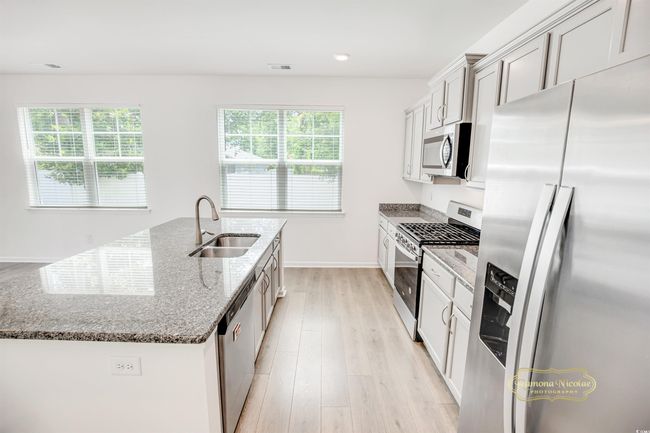 Kitchen with stainless steel appliances, a sink, an island with sink, dark stone counters, and light wood-type flooring | Image 11